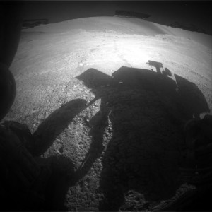 Opportunity Mars rover’s Rear Hazcam Sol 4323 image shows shadow and tracks of the veteran robot, taken on March 22, 2016. The hillside descends to the left into “Marathon Valley.” The floor of Endeavour Crater is seen beneath the underside of a solar panel. Credit: NASA/JPL-Caltech 